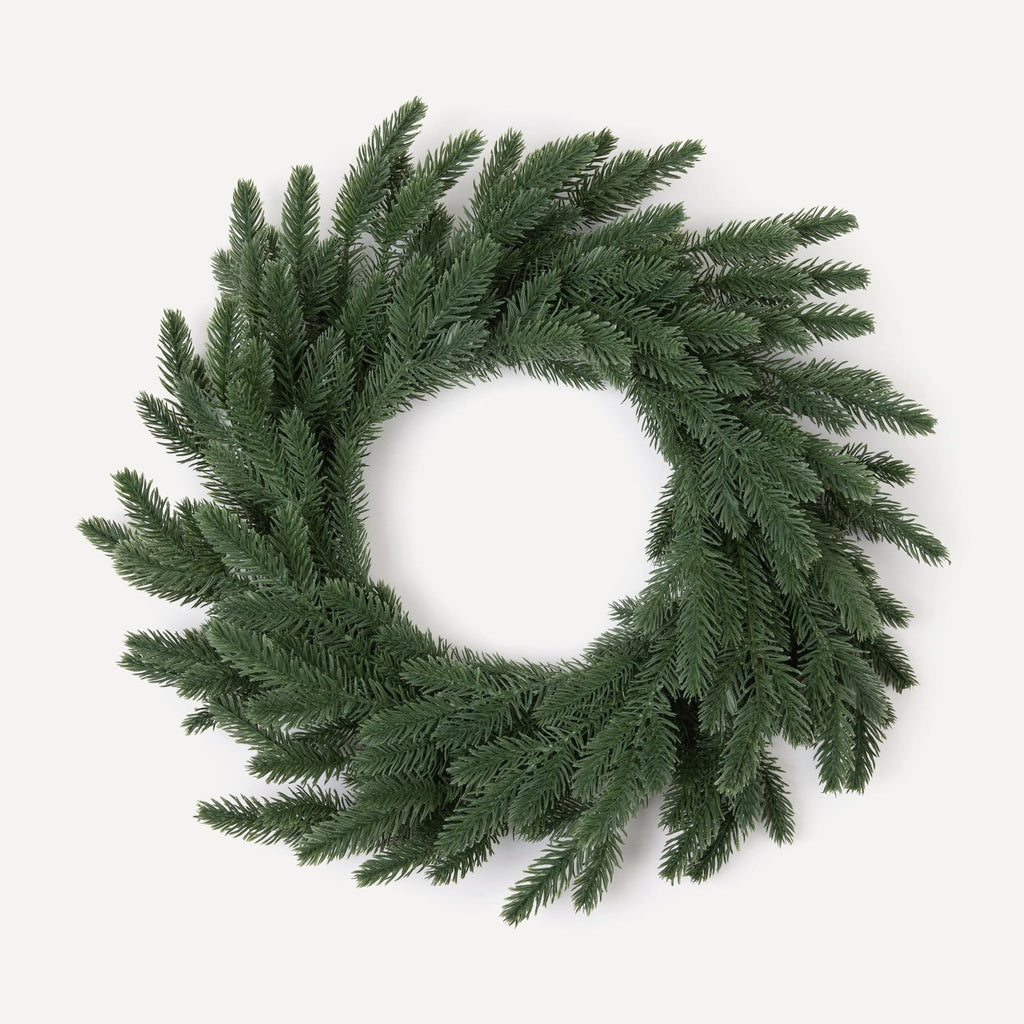A round, green Christmas wreath made of artificial pine needles, hand-wrapped and displayed against a white background.
