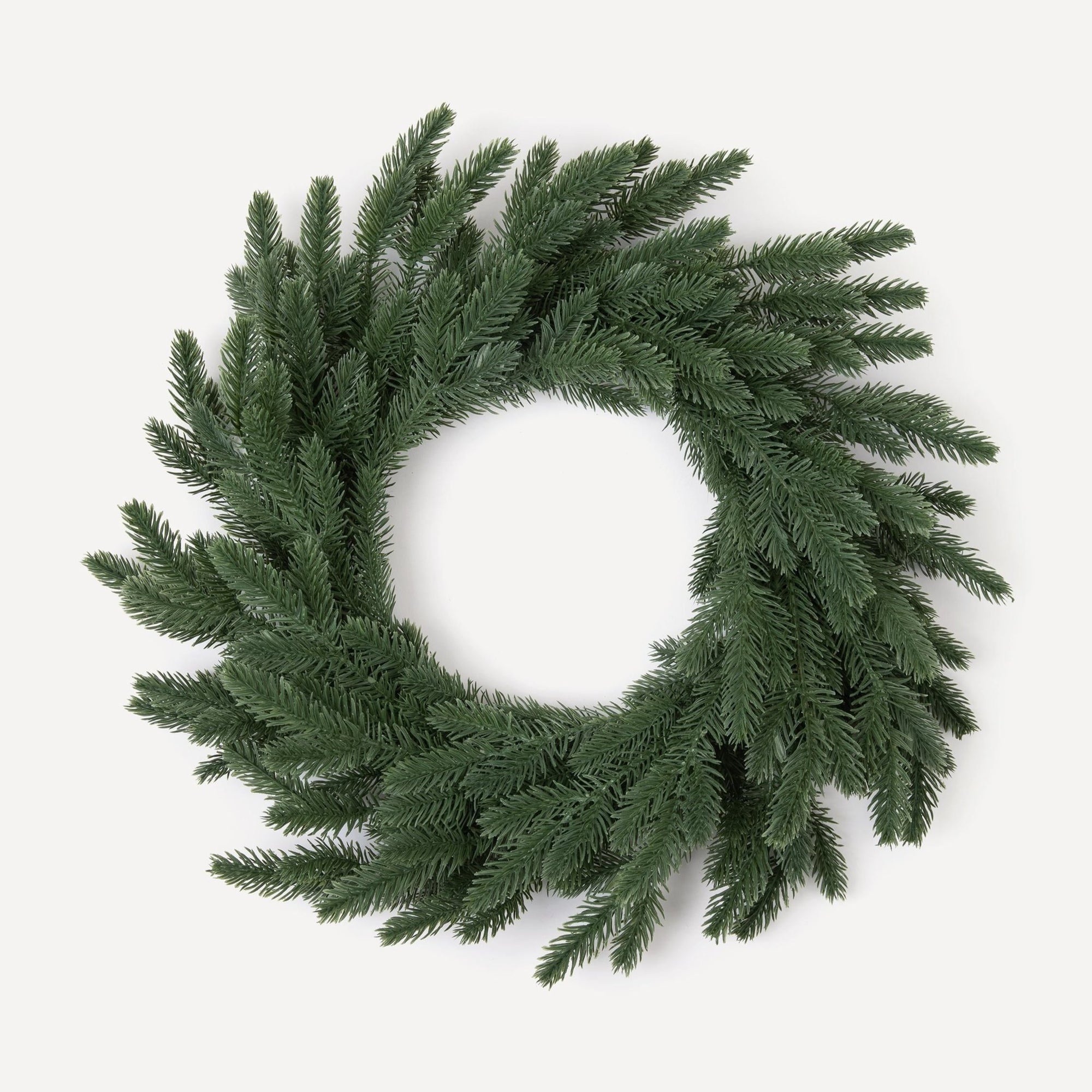 A round, green Christmas wreath made of artificial pine needles, hand-wrapped and displayed against a white background.