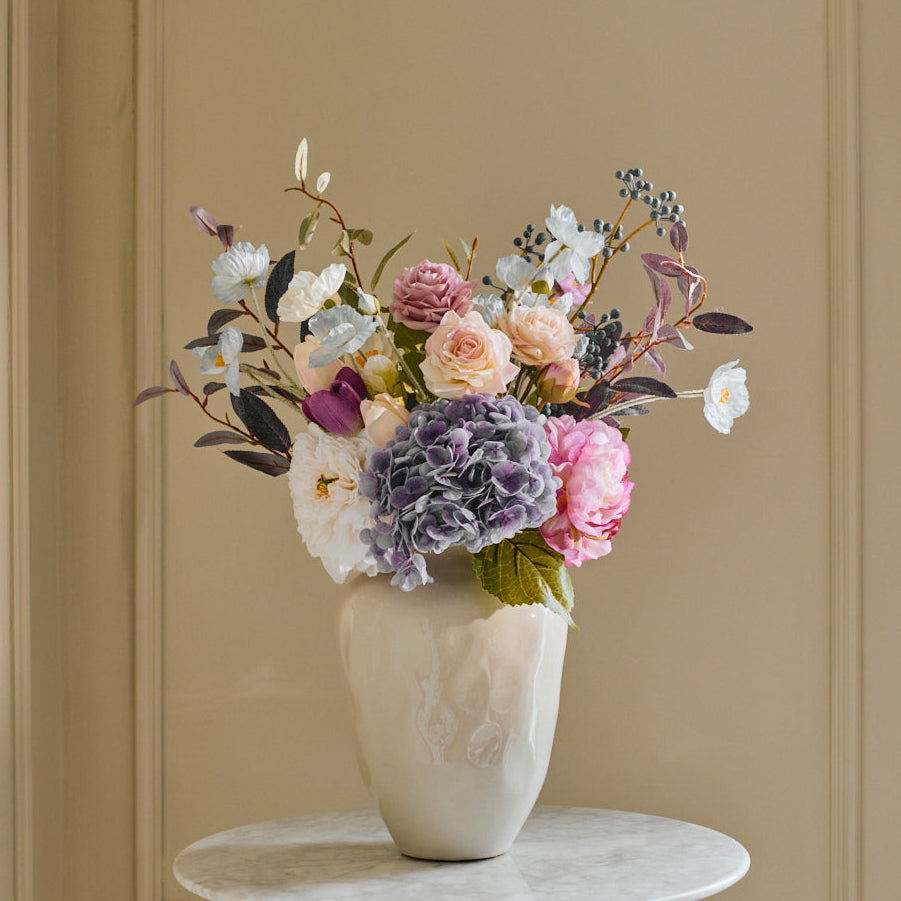 Floral arrangement in a white vase on a small round table against a beige wall.