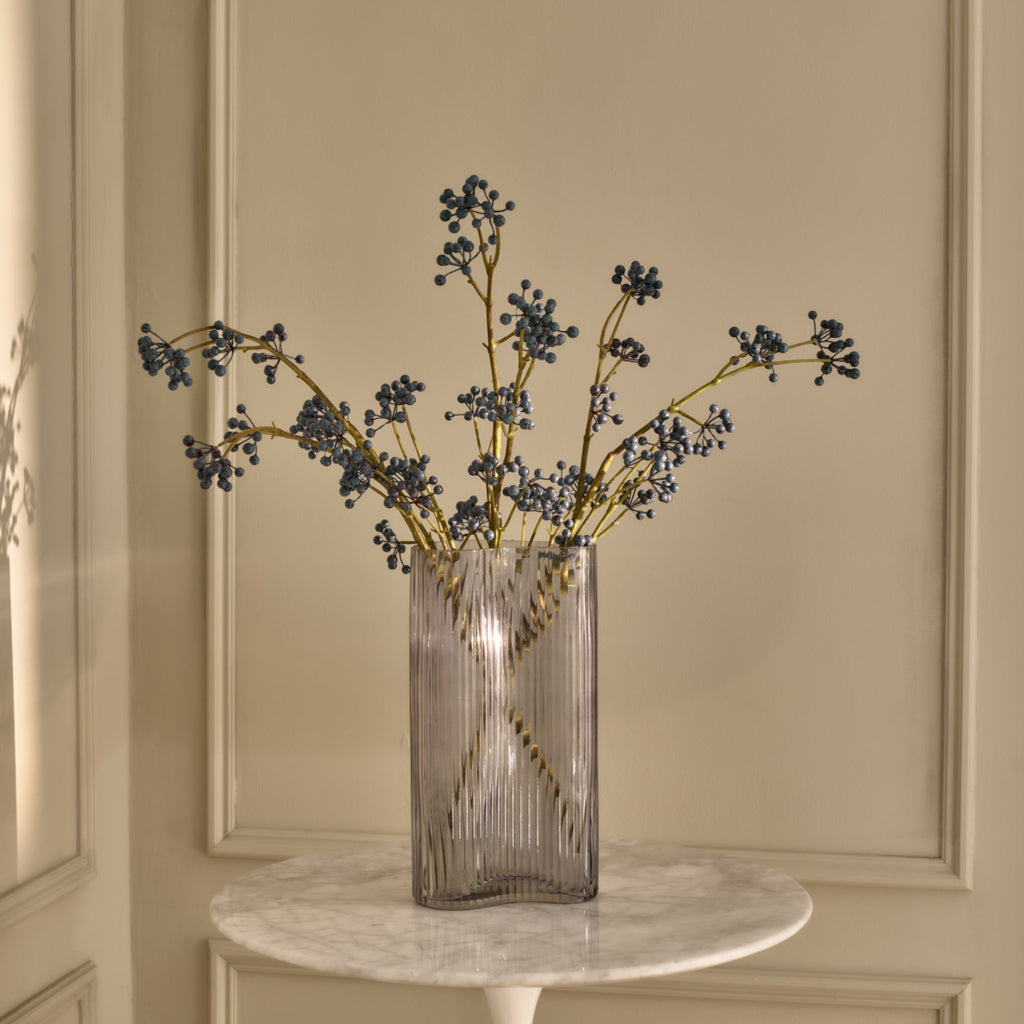 Glass vase with decorative branches on a marble table against a beige wall.