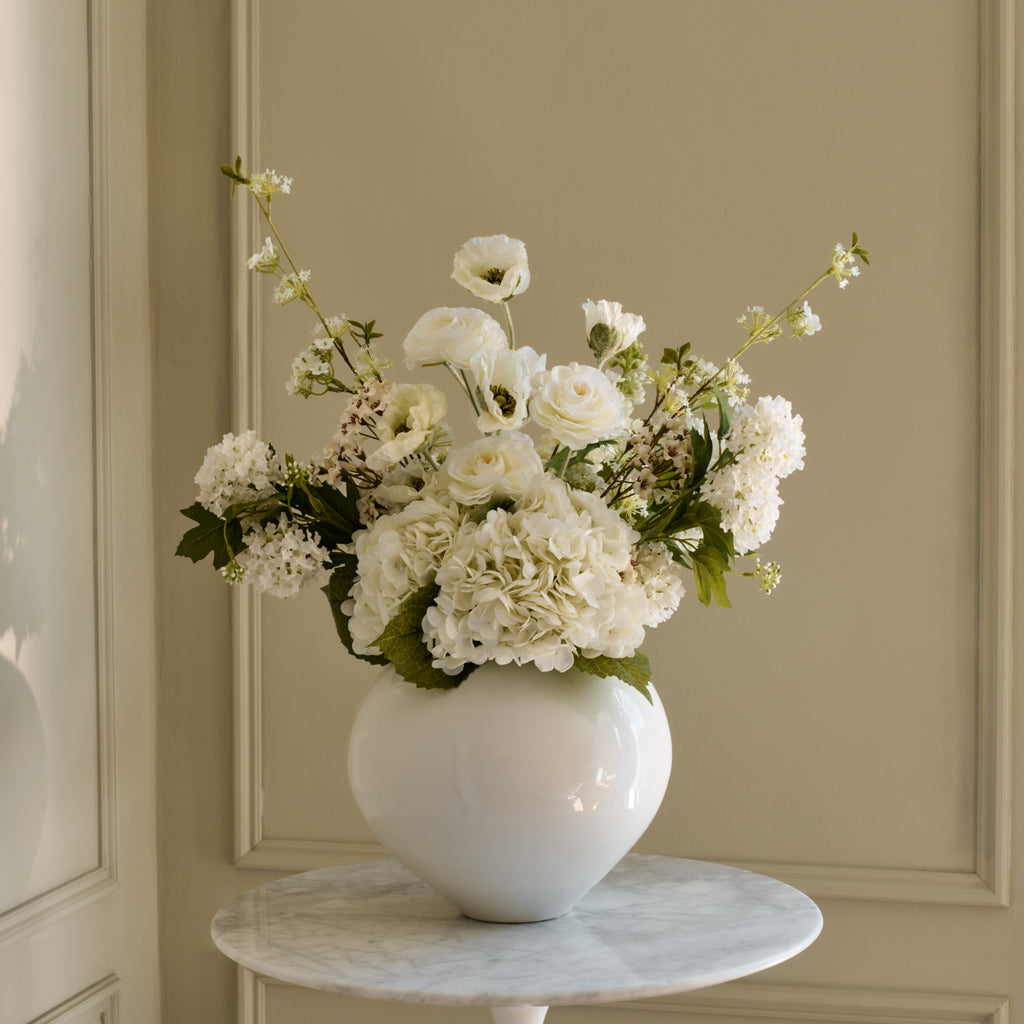 White vase with flowers on a marble side table against a beige paneled wall