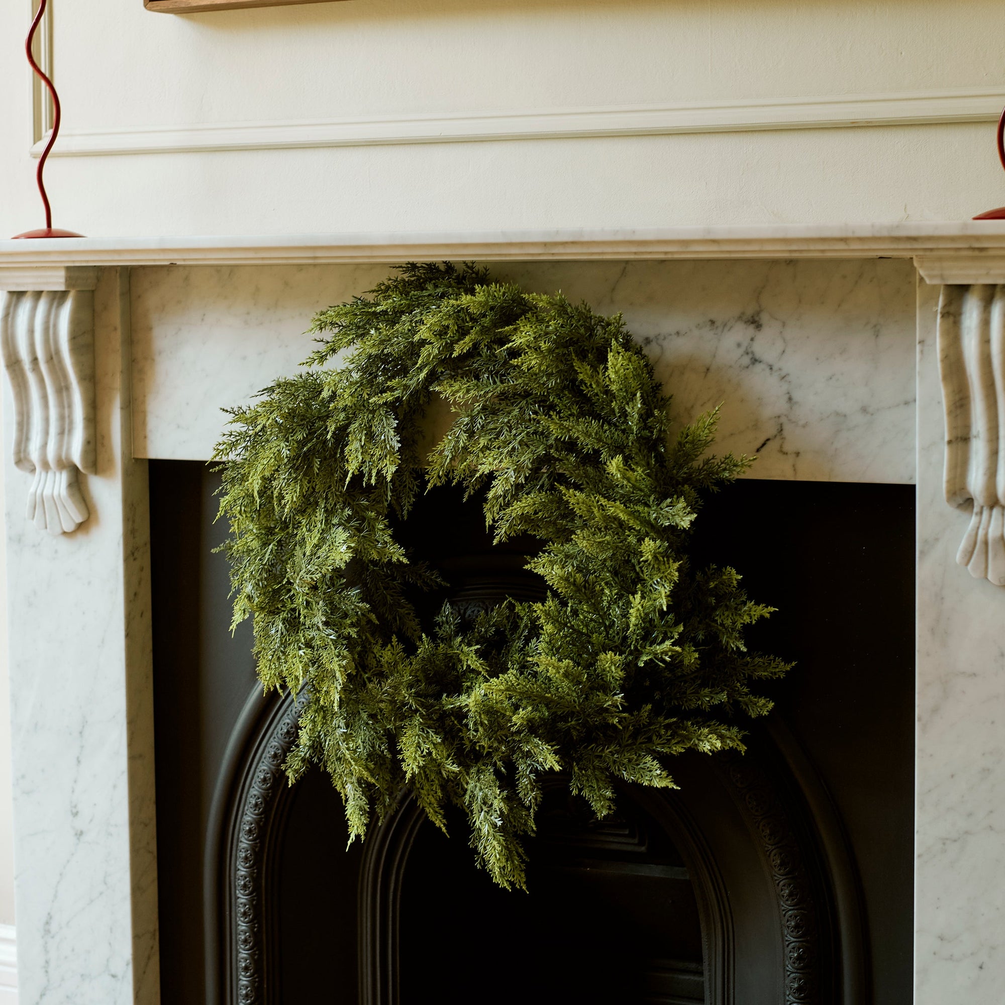 A green pine wreath hangs on a black fireplace insert beneath a white marble mantel, with a large abstract painting above and decorative candle holders on either side.