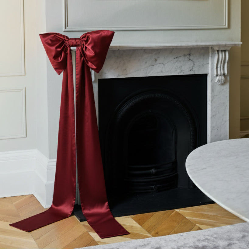 Red satin bow on a fireplace with a painting above it