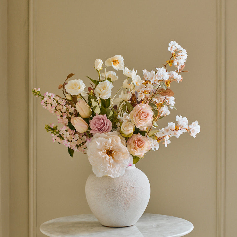 Bouquet of flowers in a white vase on a marble table against a paneled wall.