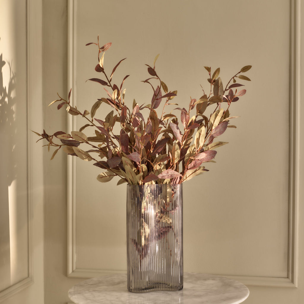 Glass vase with dried plants on a marble surface against a beige wall