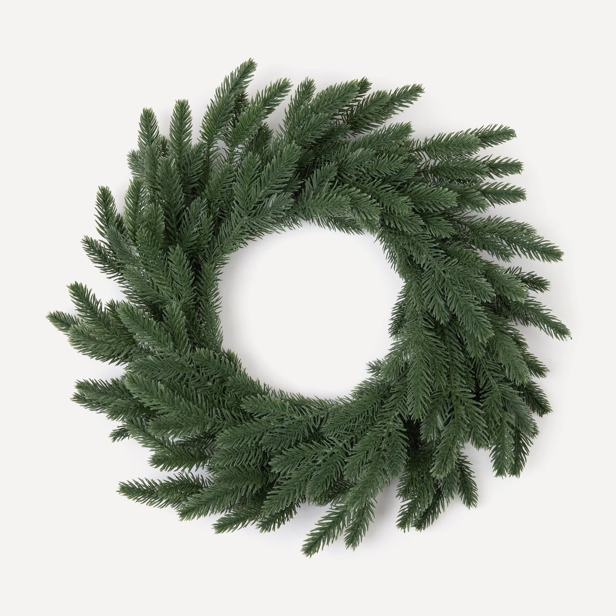 A round, green Christmas wreath made of artificial pine needles, hand-wrapped and displayed against a white background.