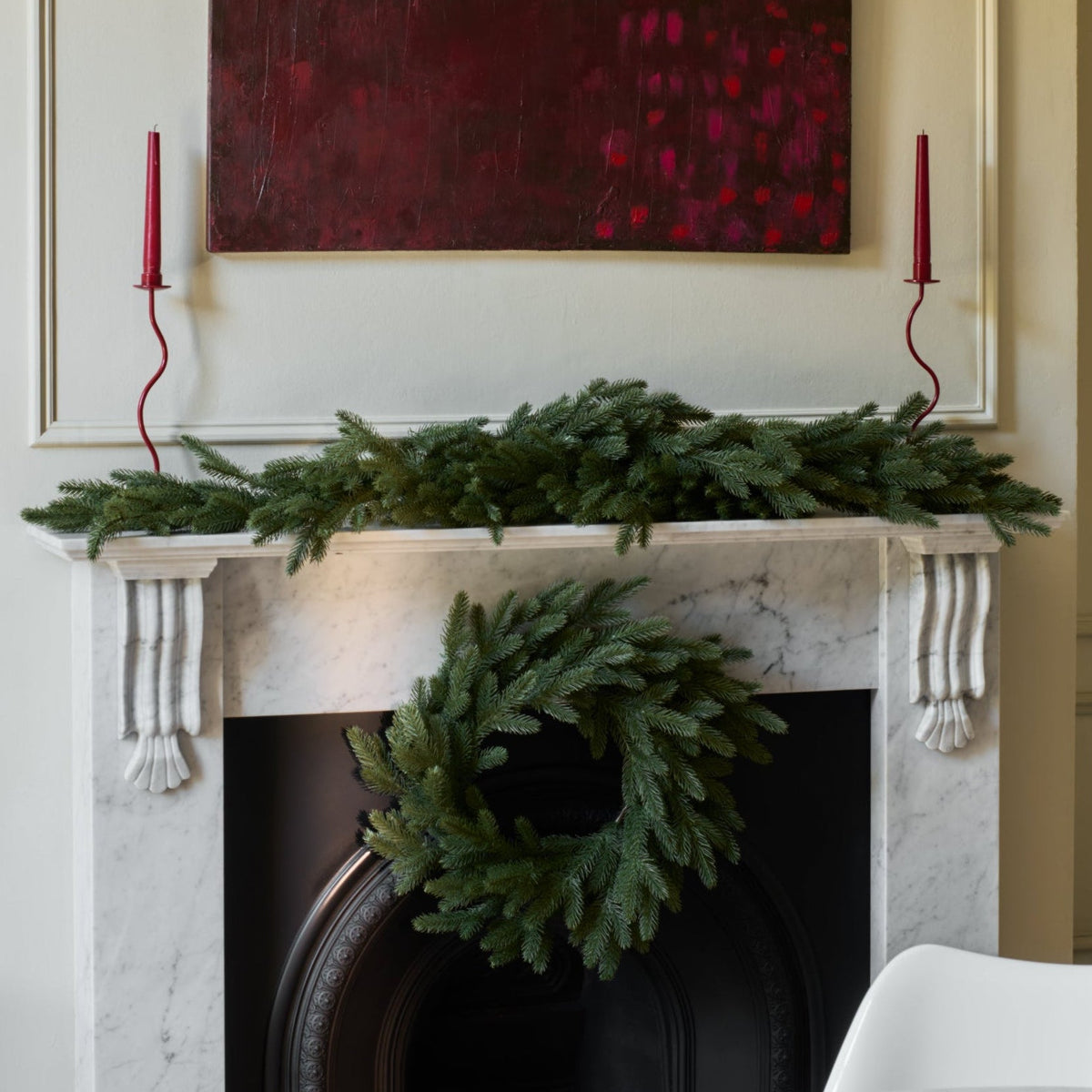 Decorative fireplace with wreath, candles, and artwork in a room.