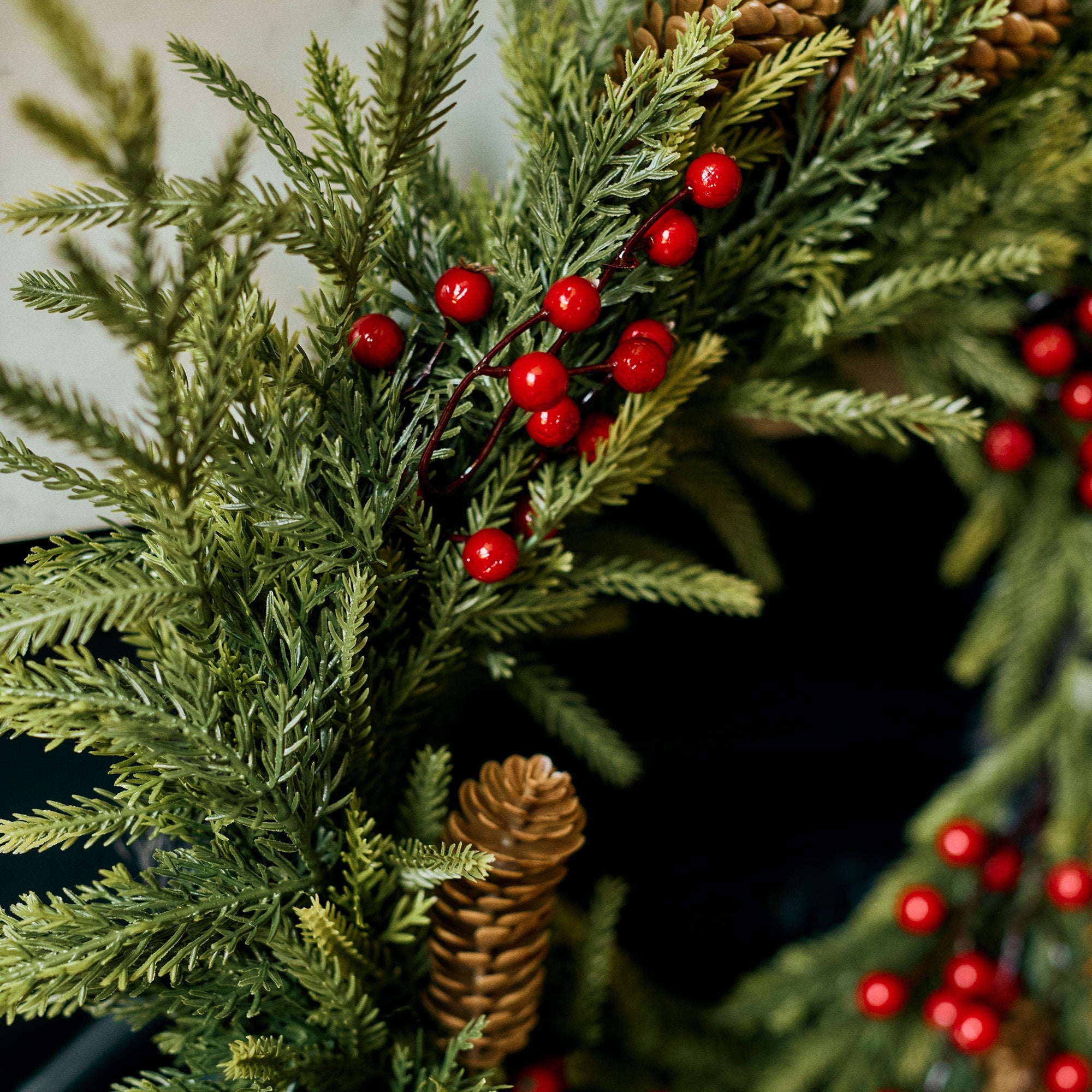 A close-up of a green evergreen wreath decorated with small red berries and natural pinecones.