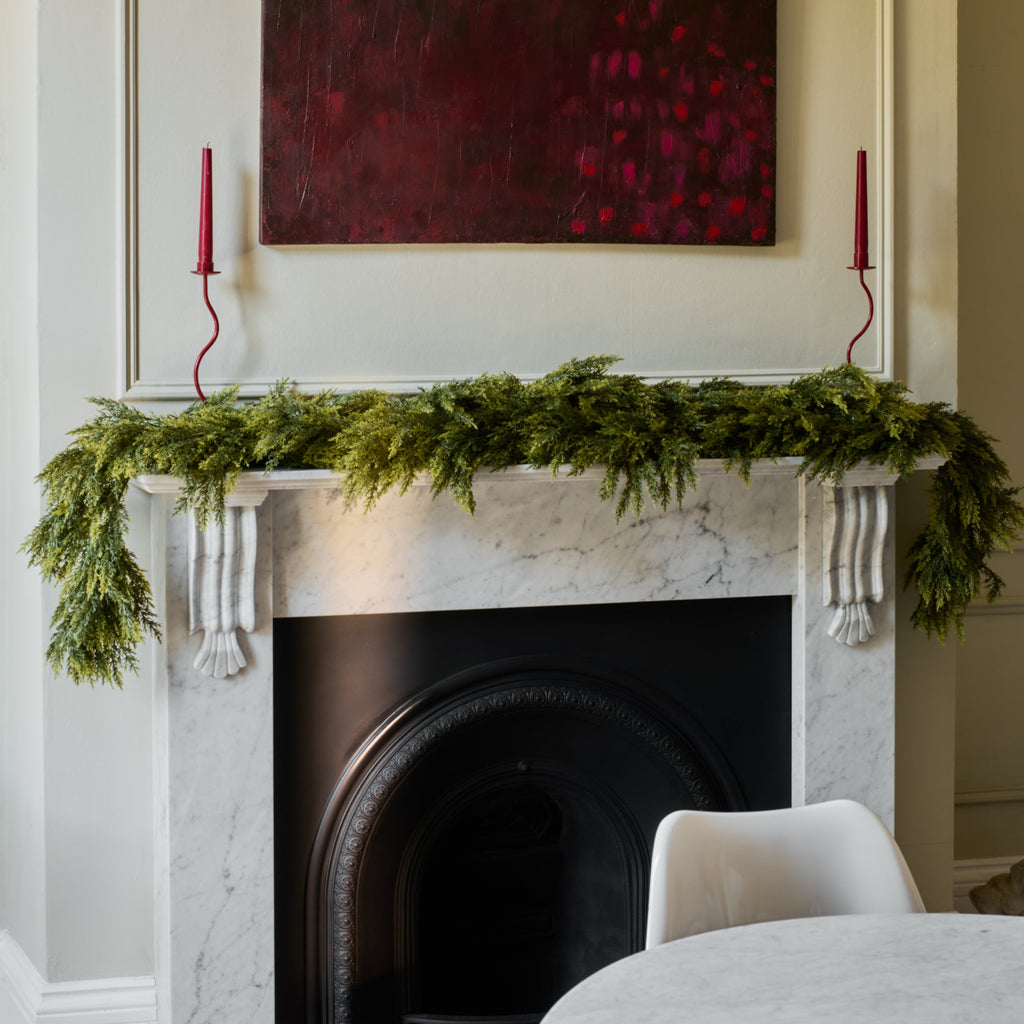 Decorative fireplace with greenery, candles, and a painting in a room.