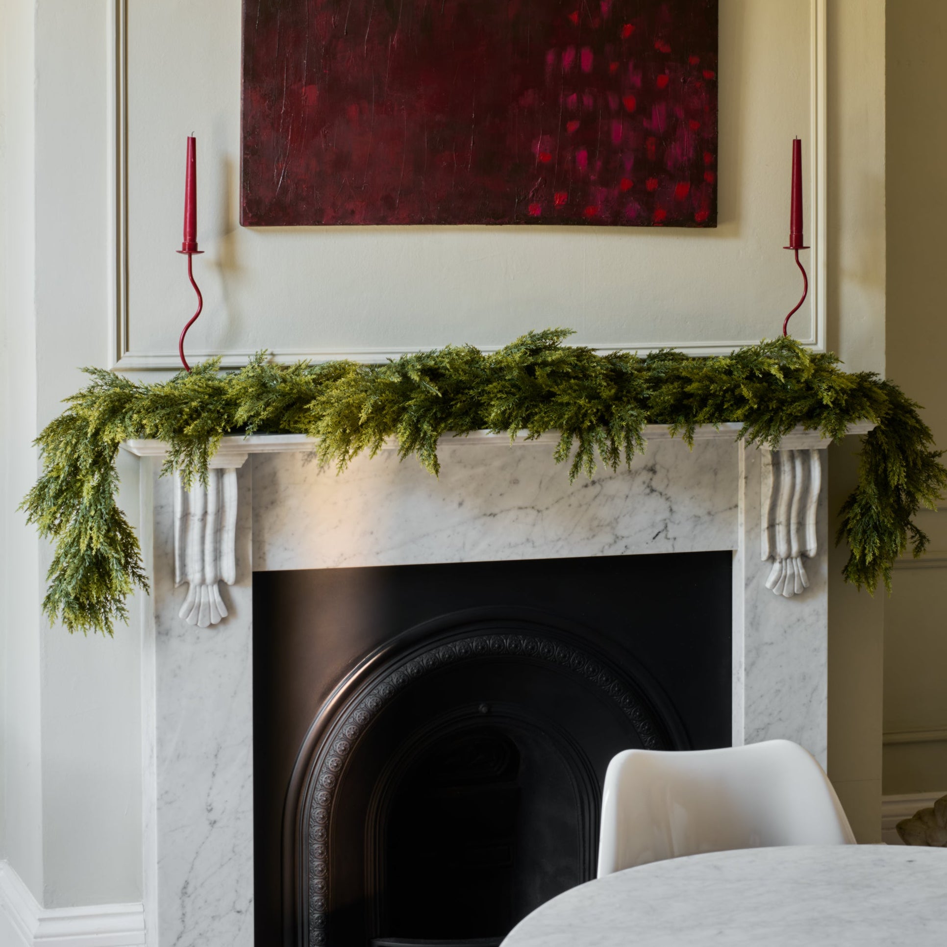 Decorative fireplace with greenery, candles, and a painting in a room.
