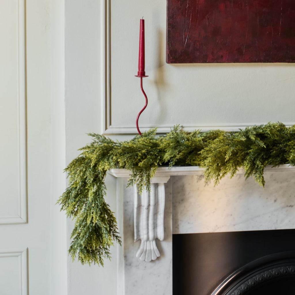 Green garland on a fireplace mantel with a red candlestick