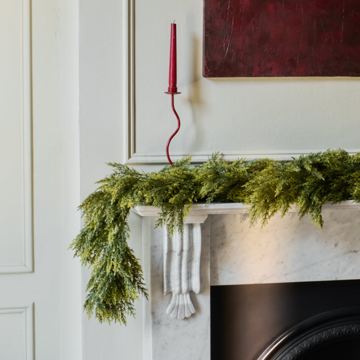 Green garland on a fireplace mantel with a red candlestick