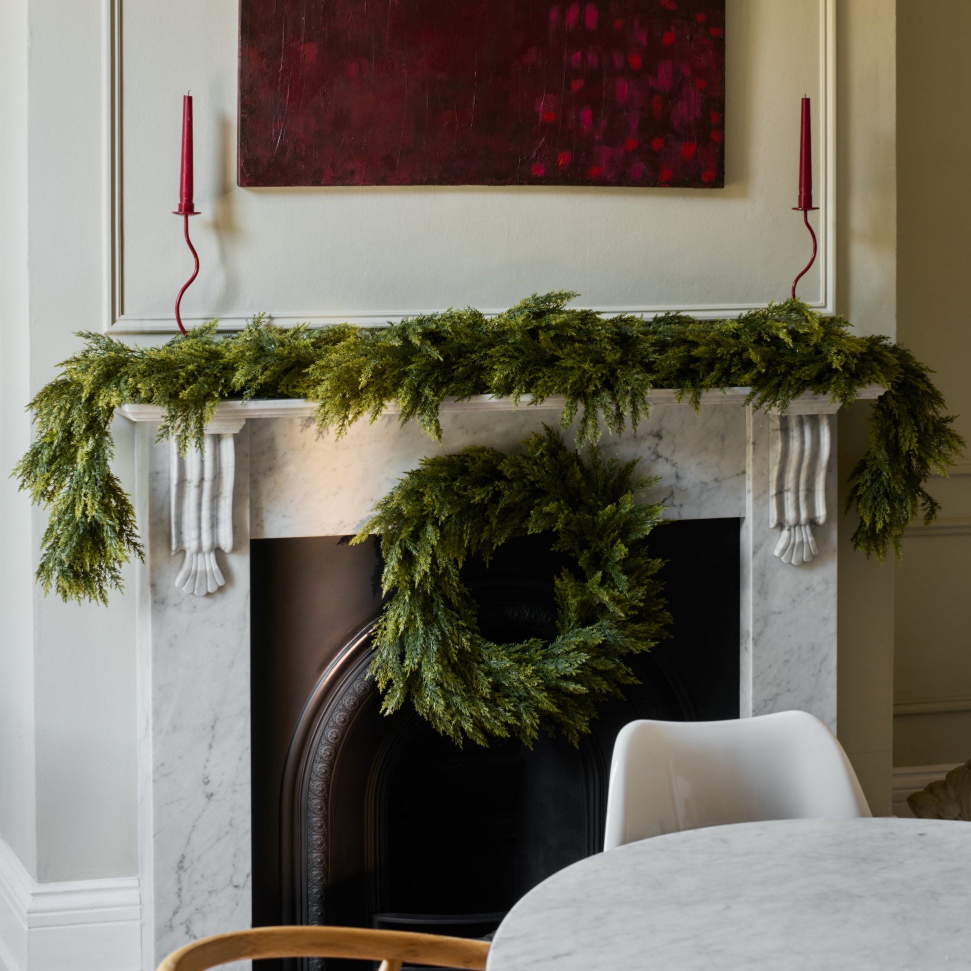 Decorative fireplace with greenery and a wreath, above which is a red abstract painting.