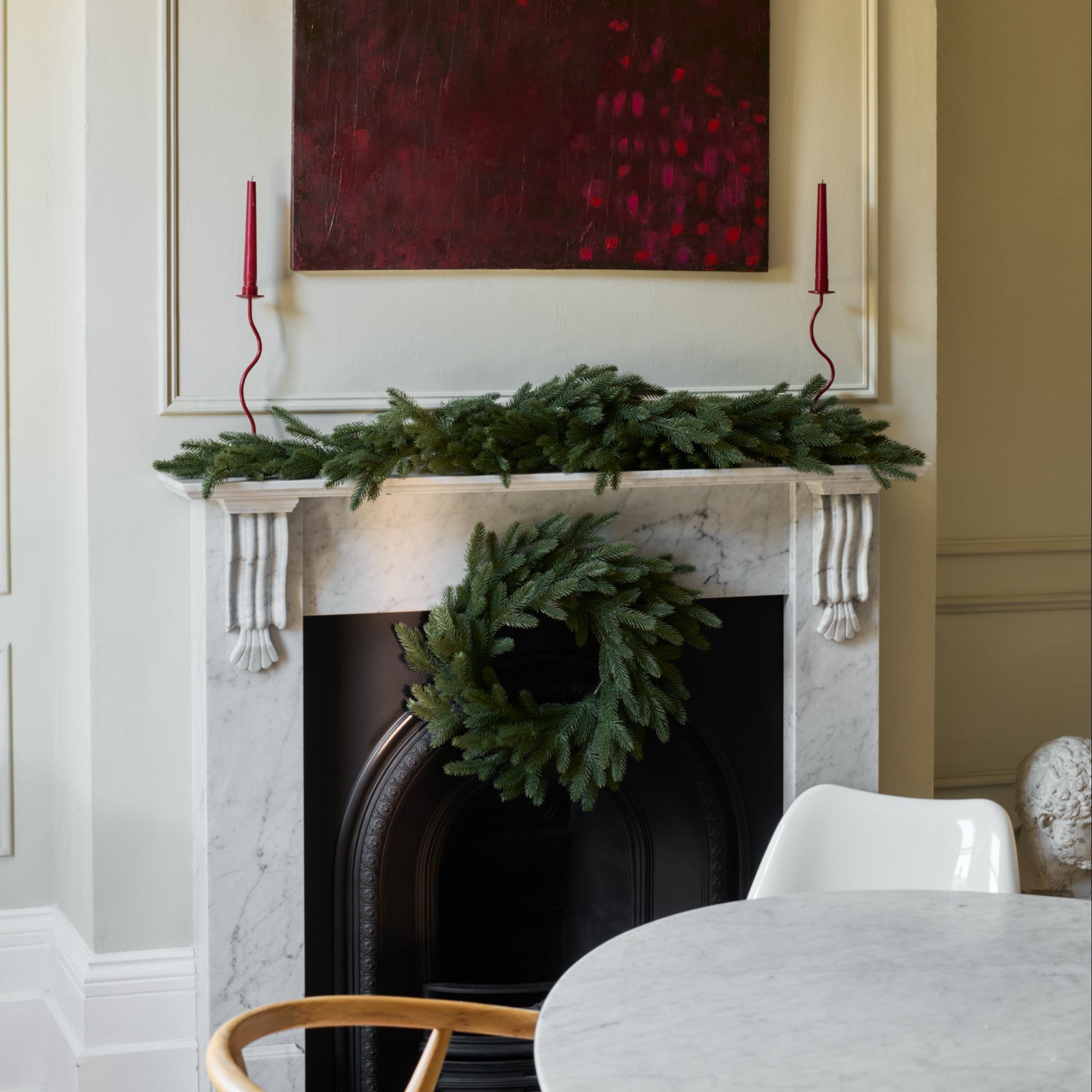 Decorative fireplace with wreath, candles, and artwork in a room.