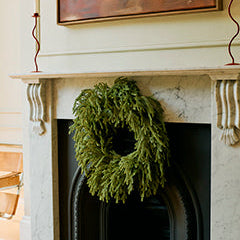 A green pine wreath holiday decoration hanging on a black fireplace insert set within a white marble mantel.
