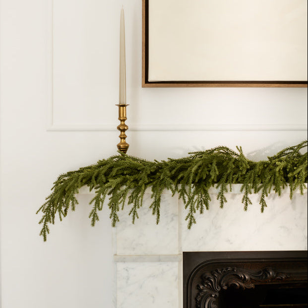Green garland on a fireplace mantel with a candle and framed picture in the background.