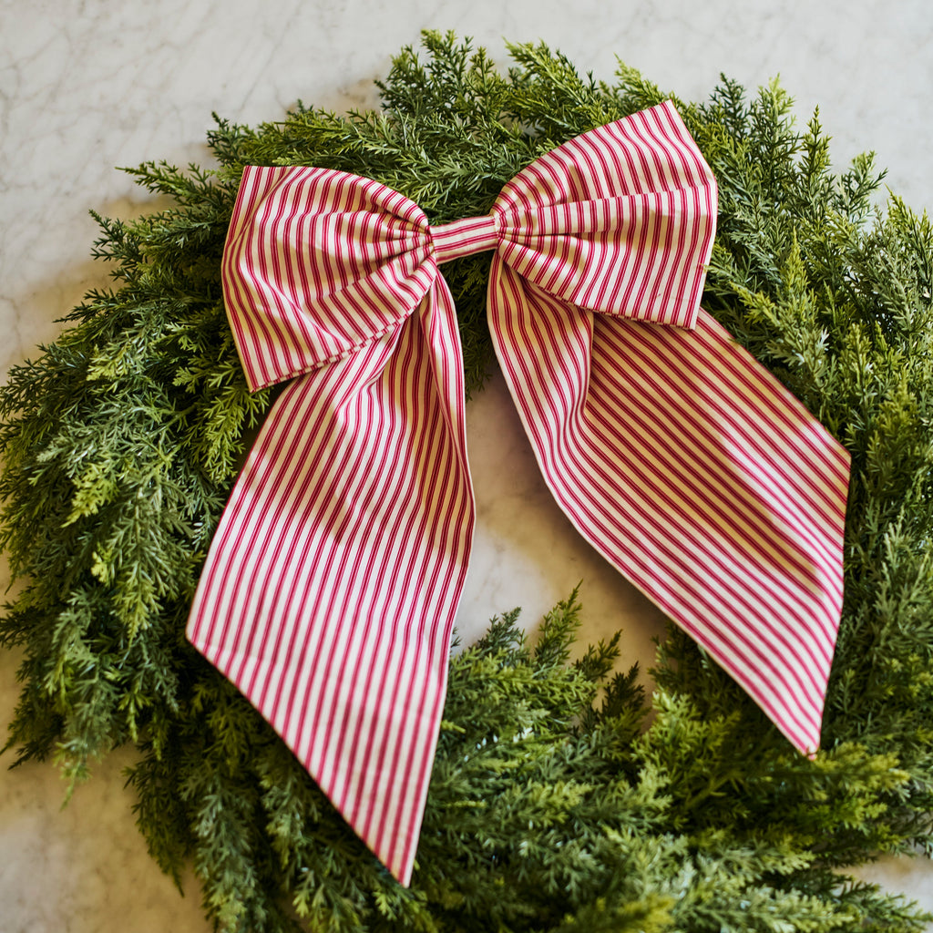 A green evergreen wreath with a large pink and white striped fabric bow, photographed on a light marble surface.