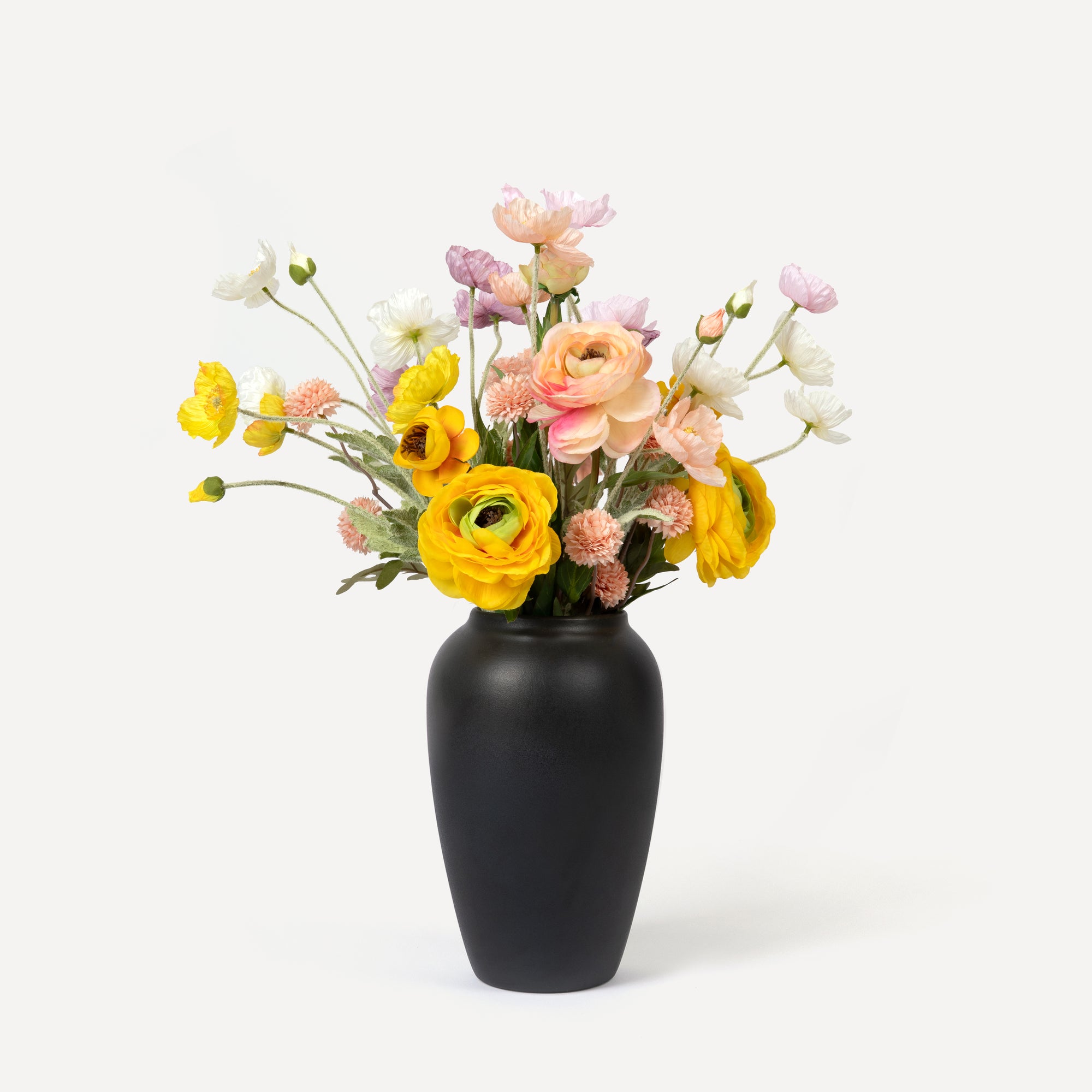 A faux flower arrangement featuring a variety of artificial flowers in yellow, white, and pink colors, displayed in a black ceramic vase.