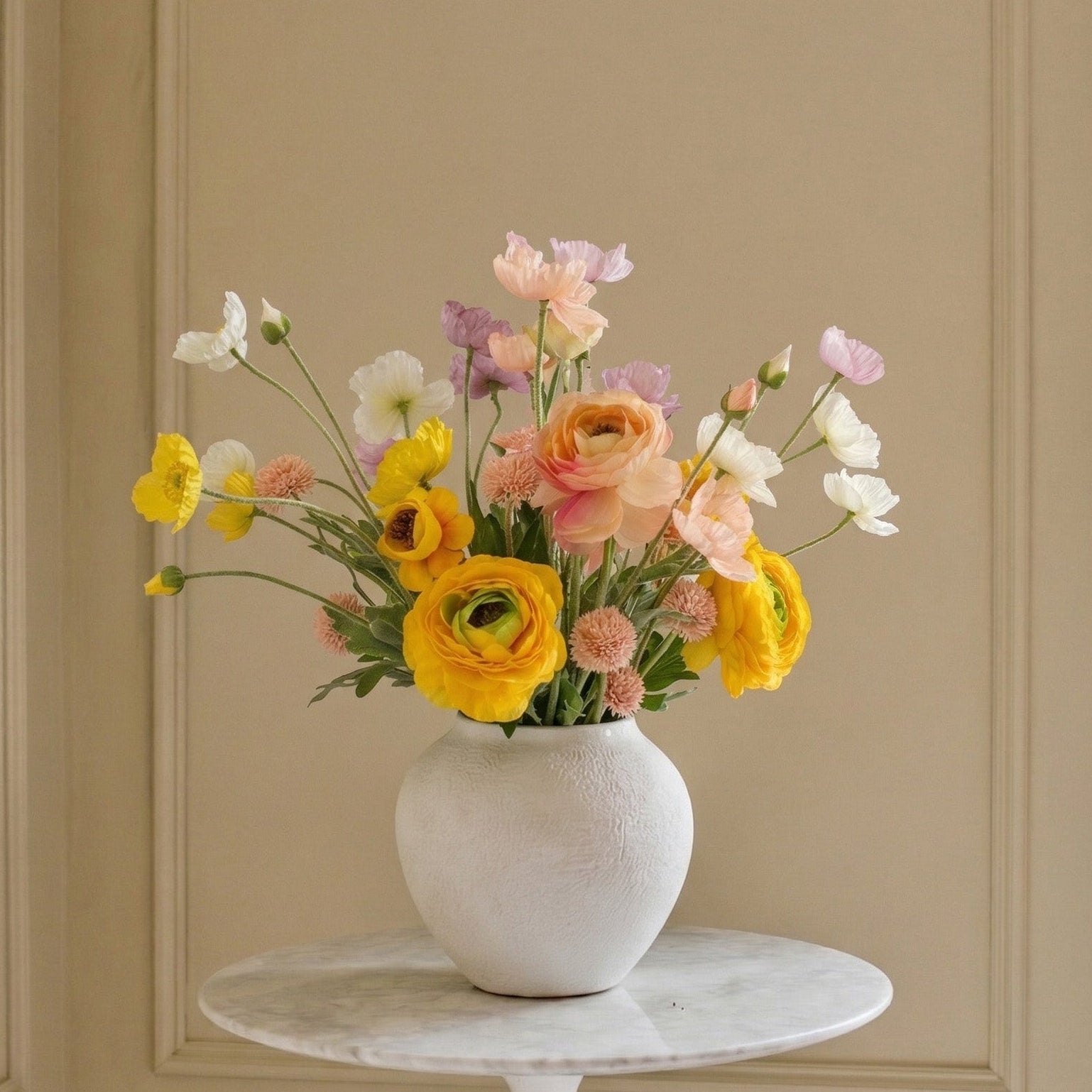 White vase with colorful flowers on a marble table against a beige wall