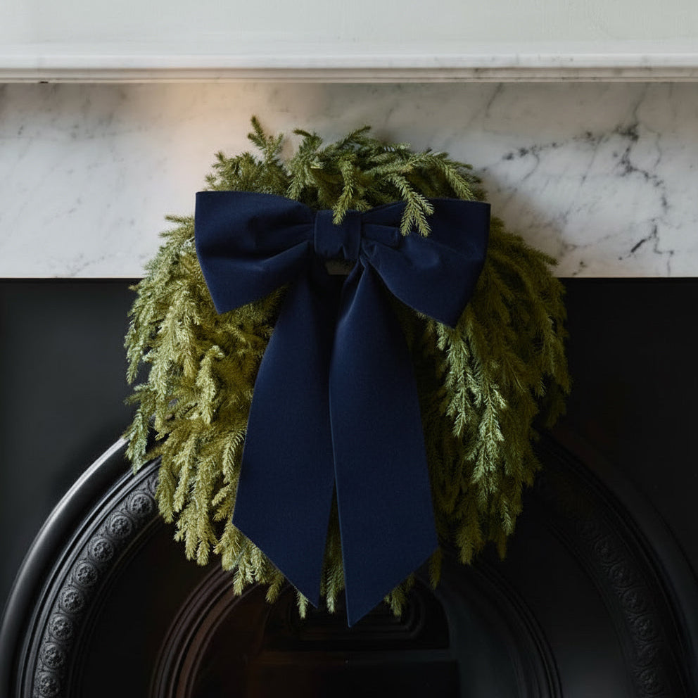 Green wreath with a navy blue bow on a fireplace mantel.