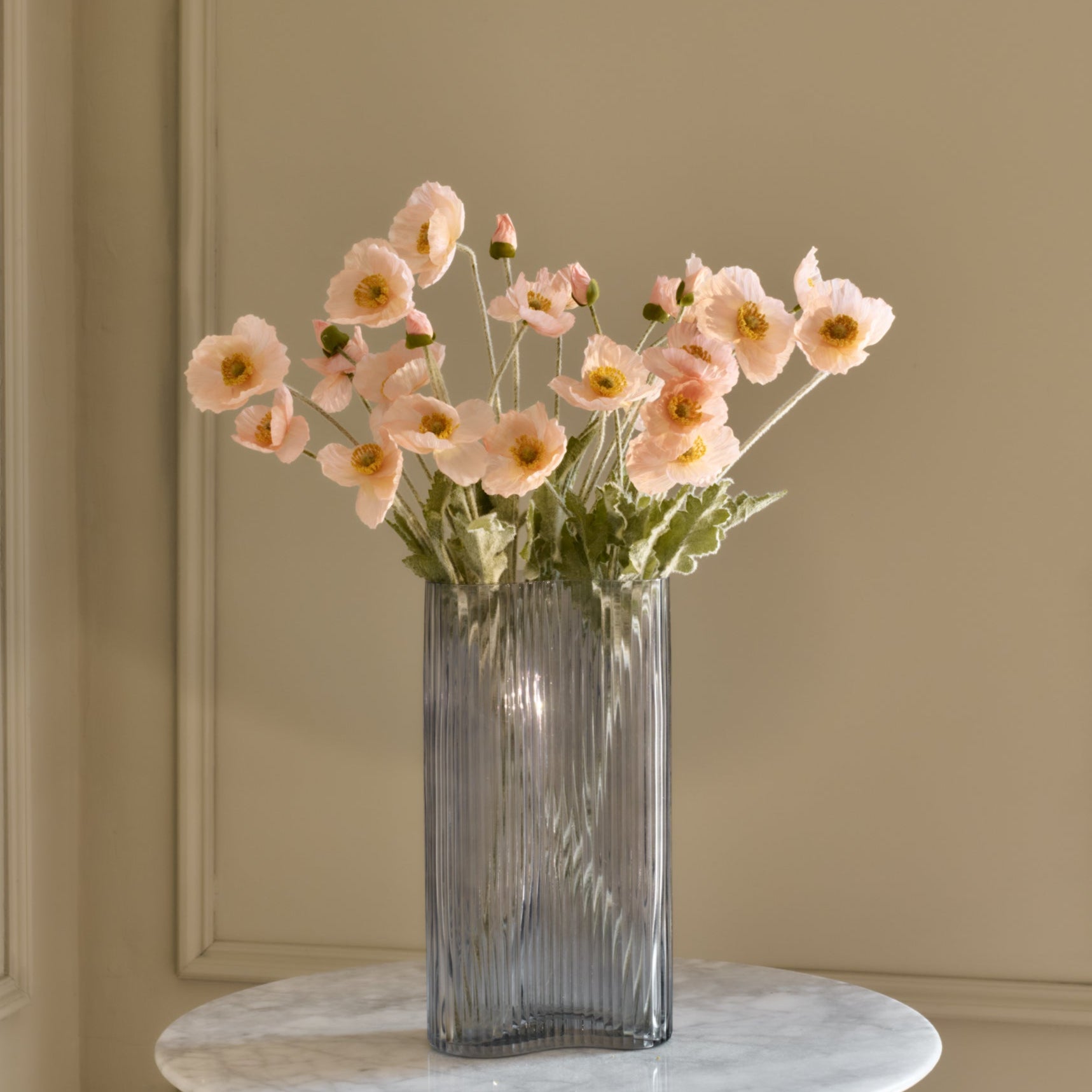 Clear glass vase with pink flowers on a marble surface against a beige wall.
