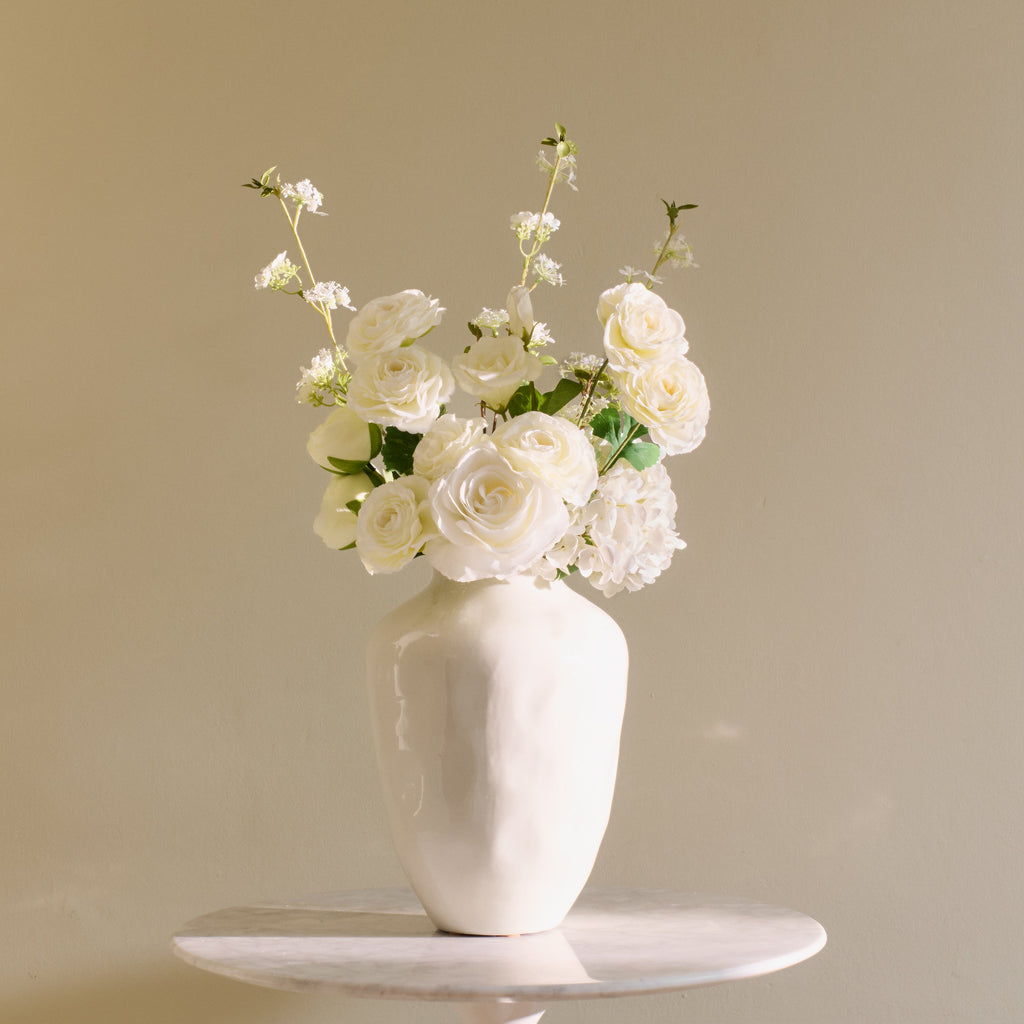 White vase with flowers on a white surface against a beige background