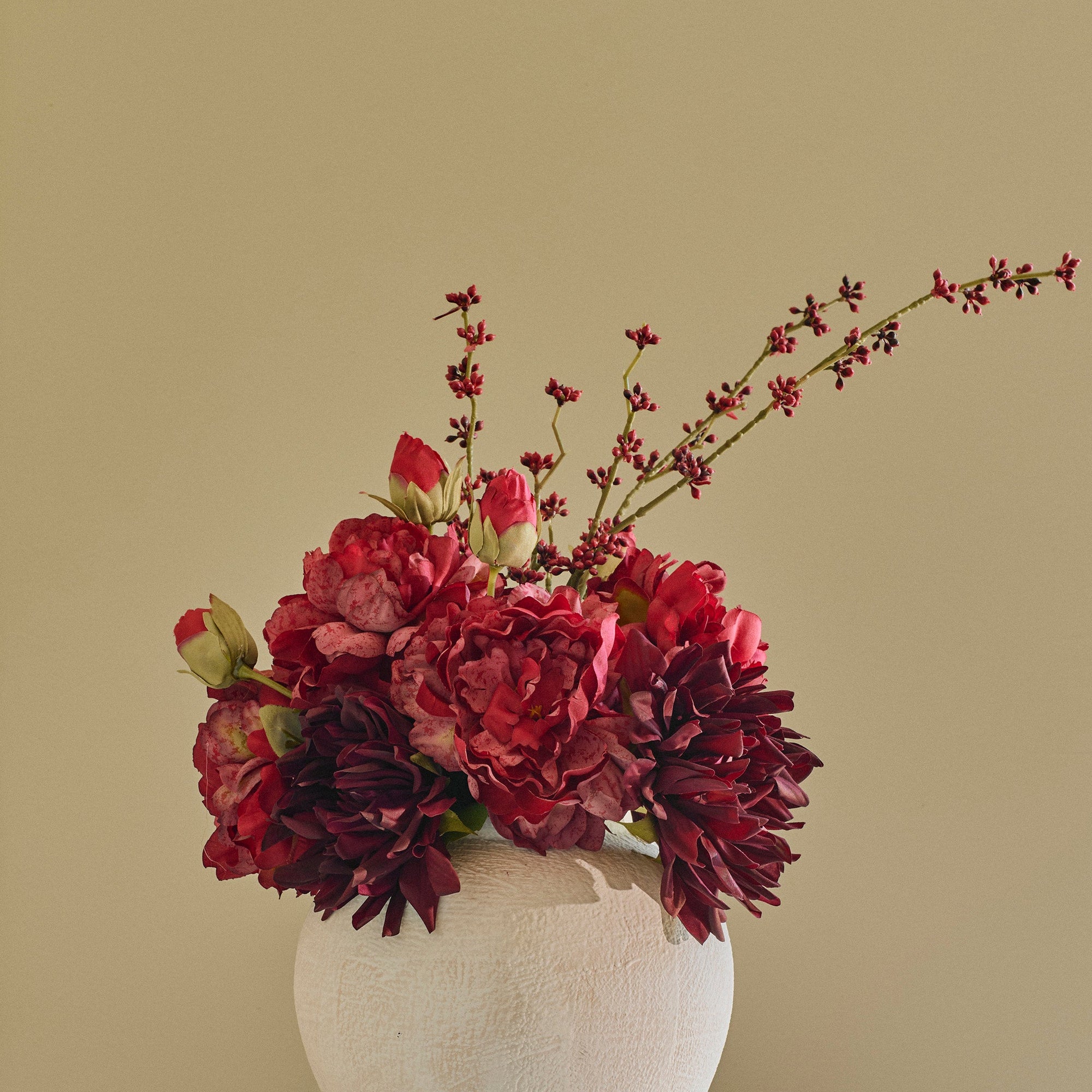 A textured off-white ceramic vase filled with deep burgundy and red floral arrangements, displayed on a round white marble side table against a beige paneled wall.