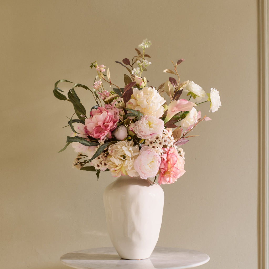 Floral arrangement in a white vase on a small round table against a beige paneled wall.