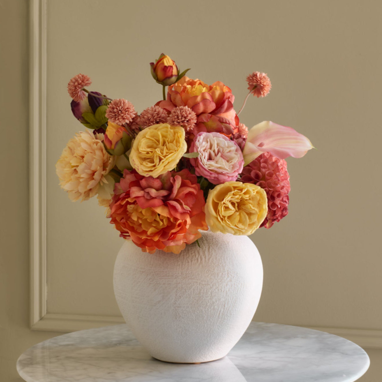 Colorful flower arrangement in a white vase on a marble surface with a beige wall background