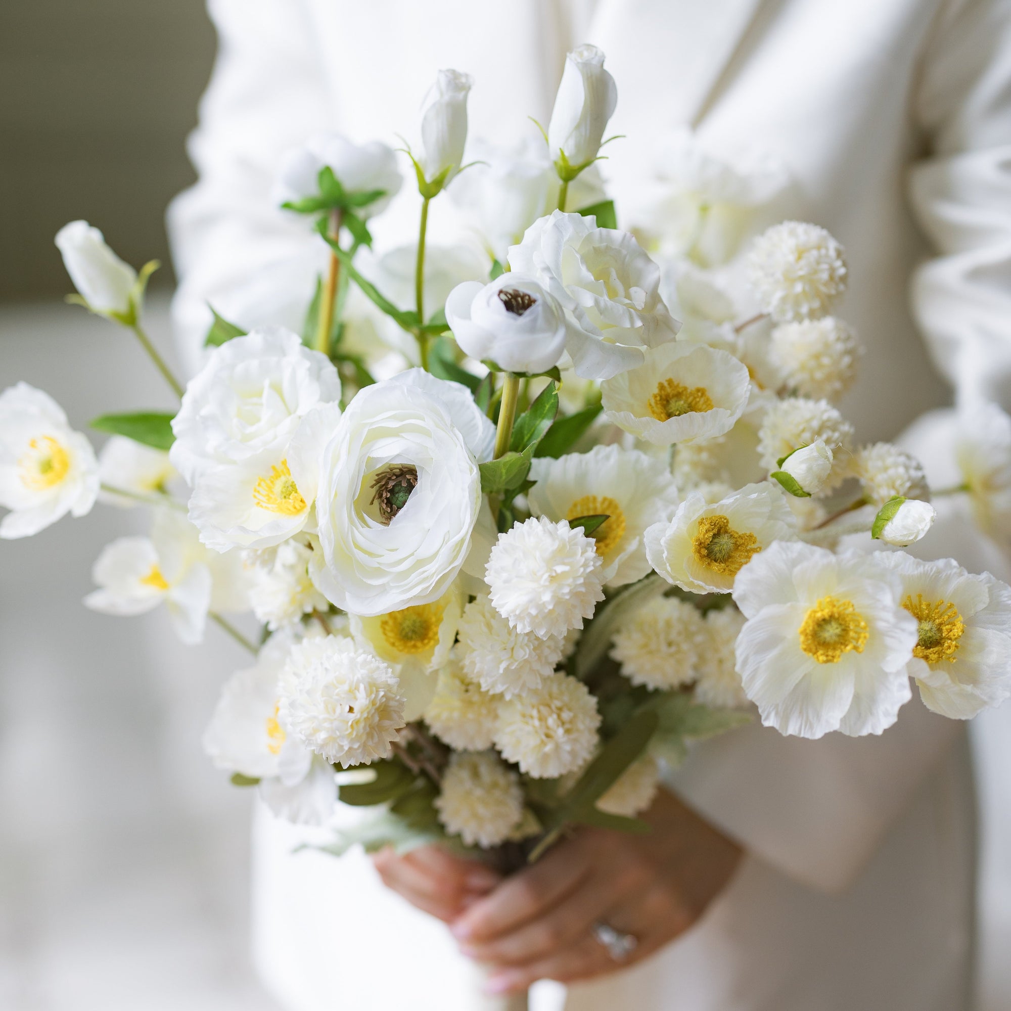 A bridal wedding bouquet consisting of white and cream flowers with green leaves, held by a person.